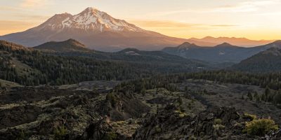 Snow-dusted mountain rising above forested ridges and rocky volcanic terrain
