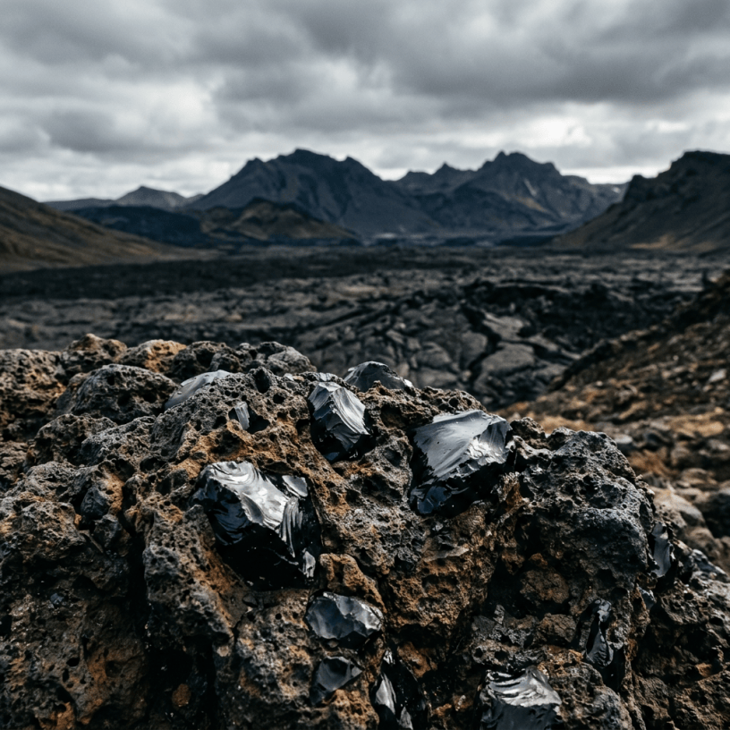 Jagged black obsidian fragments among volcanic rocks with mountains beyond